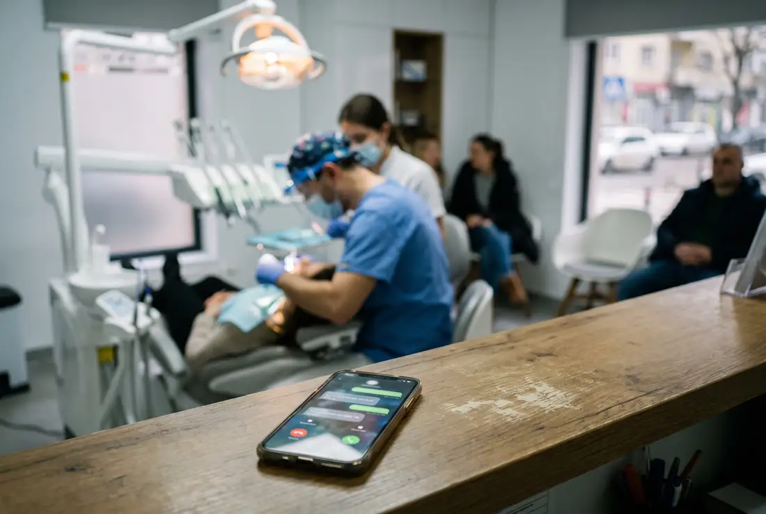 Dental clinic front desk: a phone full of notifications in the foreground, the dentist working in the background