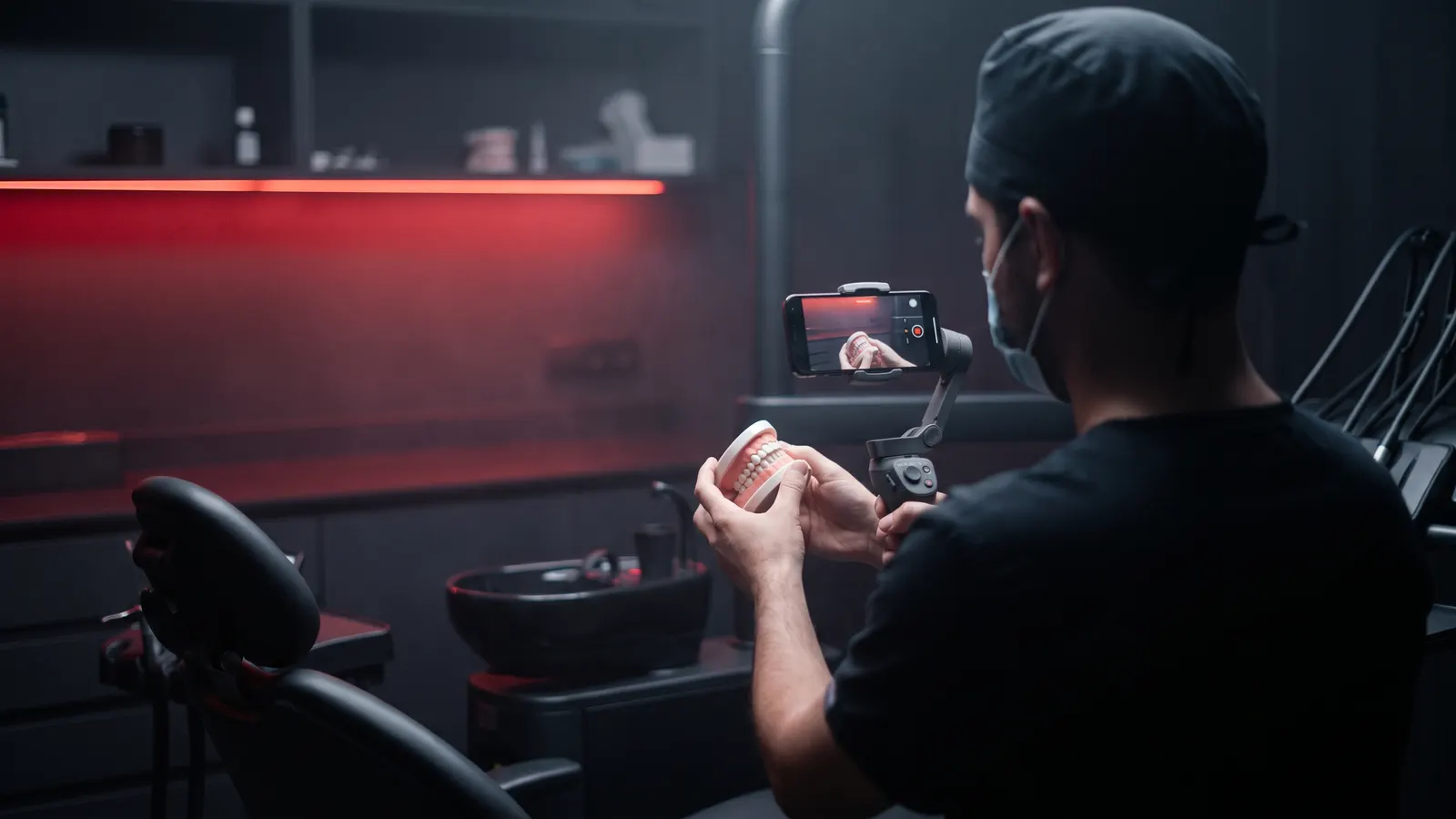 Dentist seen from behind holding a dental model while a phone on a gimbal films in a clinic