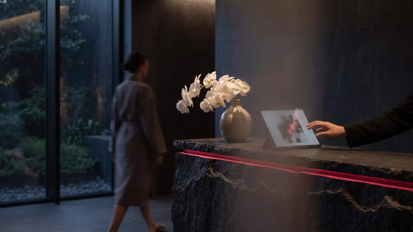 Spa reception desk with a tablet showing a booking calendar, orchids and a stone counter